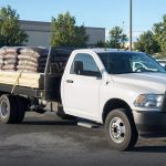 White flatbed pickup truck loaded with lumber and mulch bags in a store parking lot